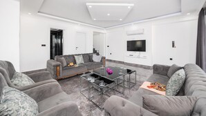 Un salon moderne avec des canapés gris, une table basse en verre et un téléviseur à écran plat fixé au mur.