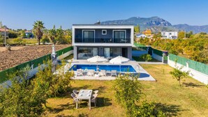 Une maison moderne à deux étages, dotée d’une piscine, d’un espace extérieur aménagé et offrant une vue sur les montagnes.