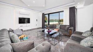 Un salon moderne avec un grand canapé, une table basse en verre et un téléviseur à écran plat fixé au mur.