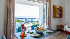 A dining area with a table set for two, a bottle of wine, a bowl of fruit, and a view of the sea. - Villa Thalia in Pilos Nestor (Messini)