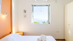 A hotel room with a bed, a window with a view, a bedside table, and a wardrobe. - Villa Thalia in Pilos Nestor (Messini)