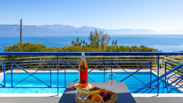 A poolside table with a bottle, glass, and fruit basket, overlooking a clear blue sea and distant mountains. - Villa Thalia in Pilos Nestor (Messini)