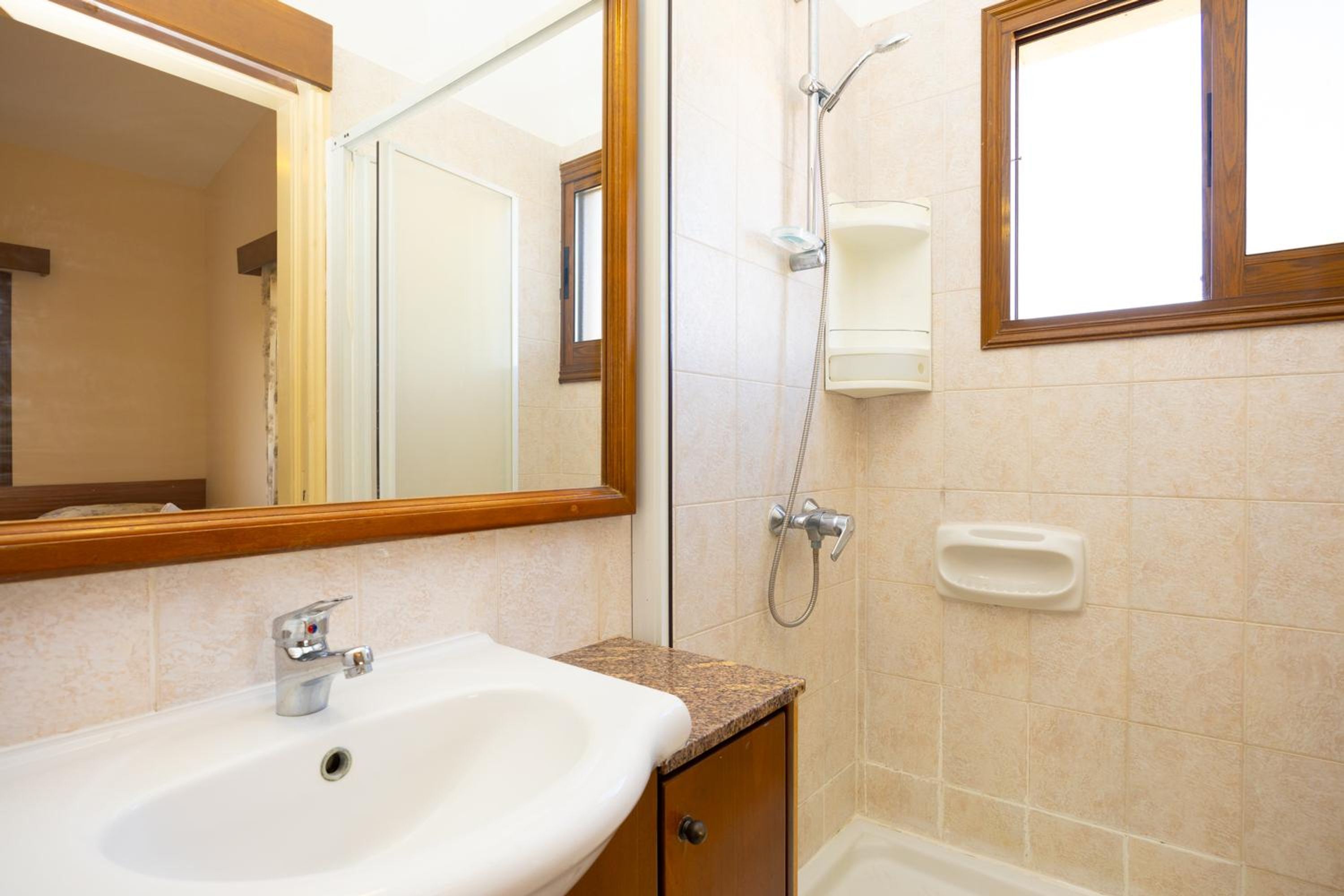 Een badkamer met een wastafel, spiegel, douche en raam.