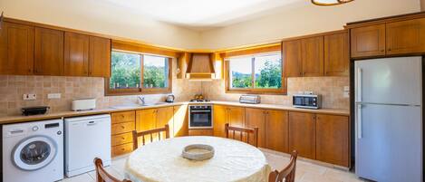 A kitchen with wooden cabinets, a washing machine, a refrigerator, and a dining table with chairs.