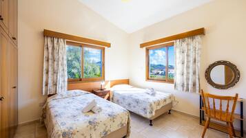A bedroom with two beds, a wooden chair, a mirror, and large windows with curtains.