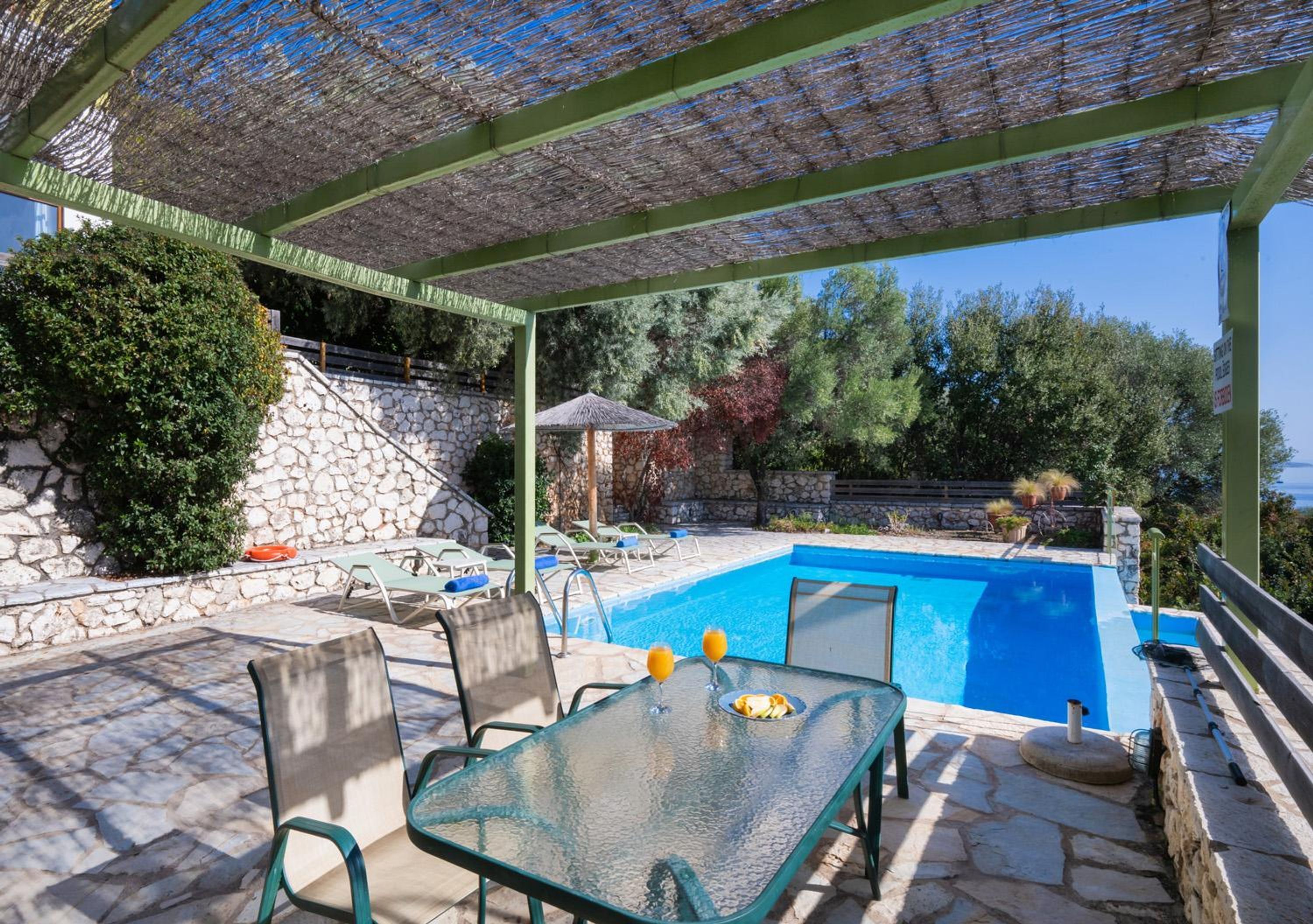 Un espace aménagé au bord de la piscine, avec une table en verre, des chaises et un mur en pierre.