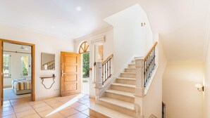 A spacious foyer with a curved staircase, a wooden door, and a mirror on the wall. - Villa Monte Rei 7 in Vila Nova de Cacela (Vila Real Santo Antonio)