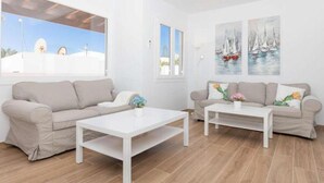 Una sala moderna con dos sofás, una mesa de centro y un ventanal con vista a un edificio blanco.