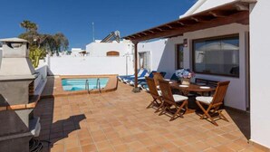 Un área de piscina en la azotea con una parrilla, sillas de descanso y una mesa de comedor.