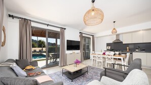 A modern living room with a sofa, coffee table, and dining area with a TV and kitchen in the background. - Villa Lidya in Dalyan (Ortaca)