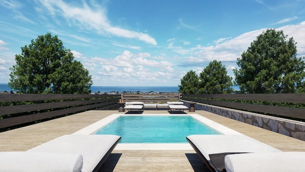 A rectangular pool with lounge chairs on either side, surrounded by a wooden deck and stone walls, with a view of the ocean and trees in the background. - Villa Liana in Spartia (Messini)