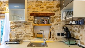 A kitchen with a stone wall, a stainless steel sink, and wooden shelves. - Villa Liana in Spartia (Messini)