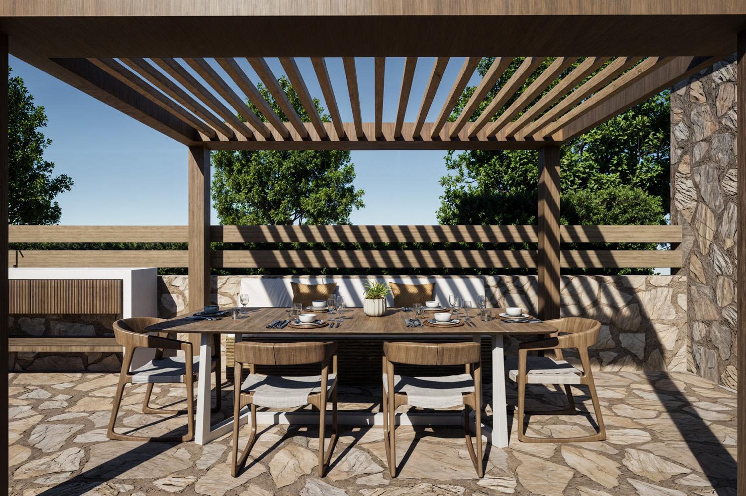An outdoor patio with a wooden pergola, stone flooring, and a round table set for dining.