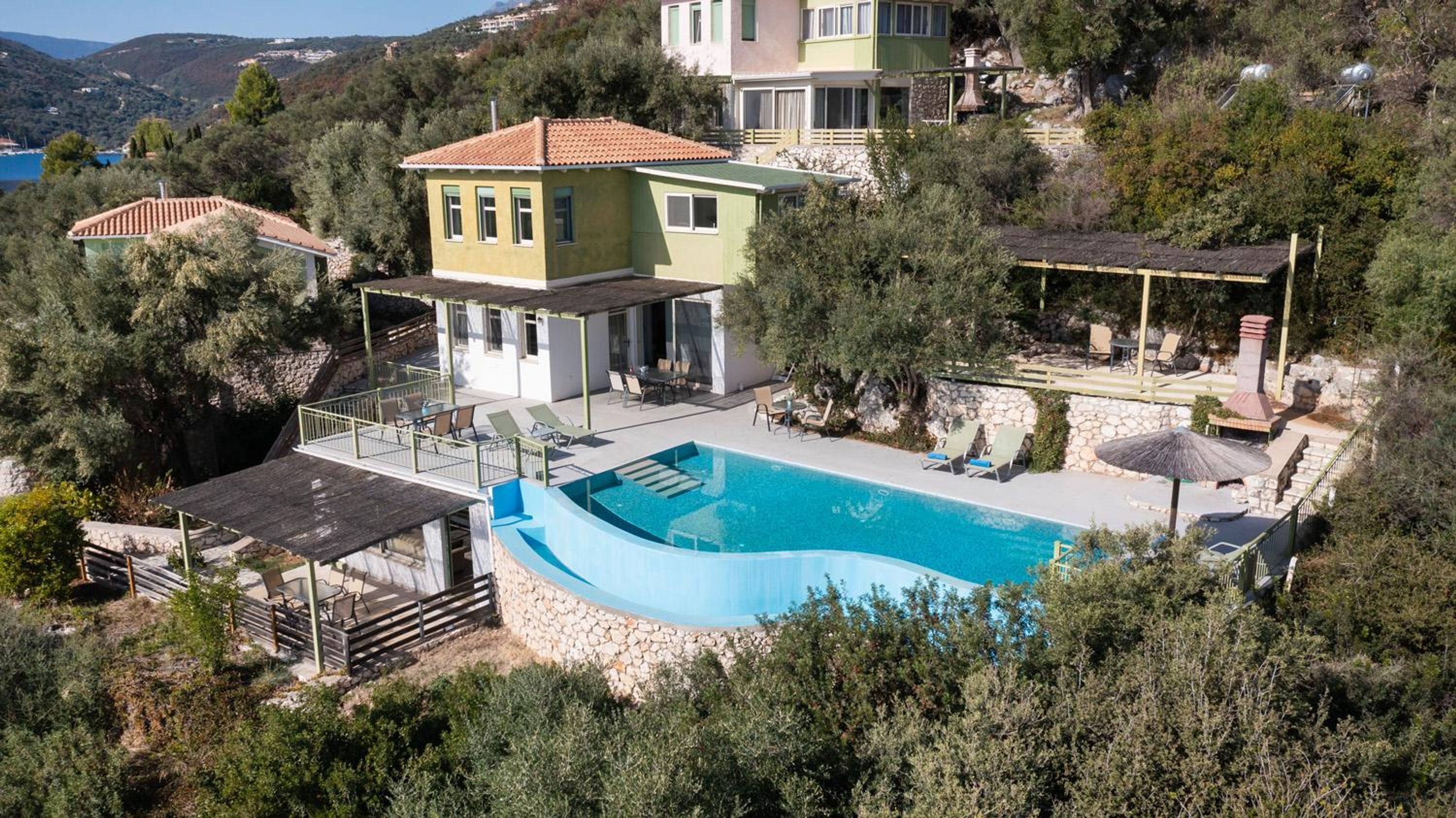 A Mediterranean-style villa with a swimming pool, outdoor seating, and a scenic hillside view.