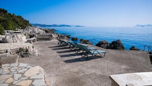 A coastal terrace with stone flooring, lounge chairs, and a view of the sea. - Villa Votsalo in Lefkada (Lefkada)