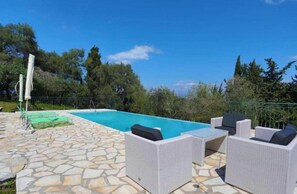 A pool area with stone flooring, outdoor furniture, and a clear blue sky. - Villa Iremia in Ionian Islands (Corfu)