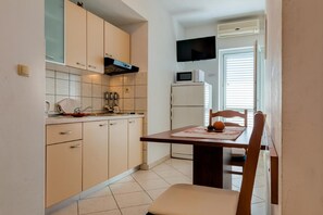 Kitchen area with microwave, refrigerator, and television, adjacent to a dining space with a table and chair.