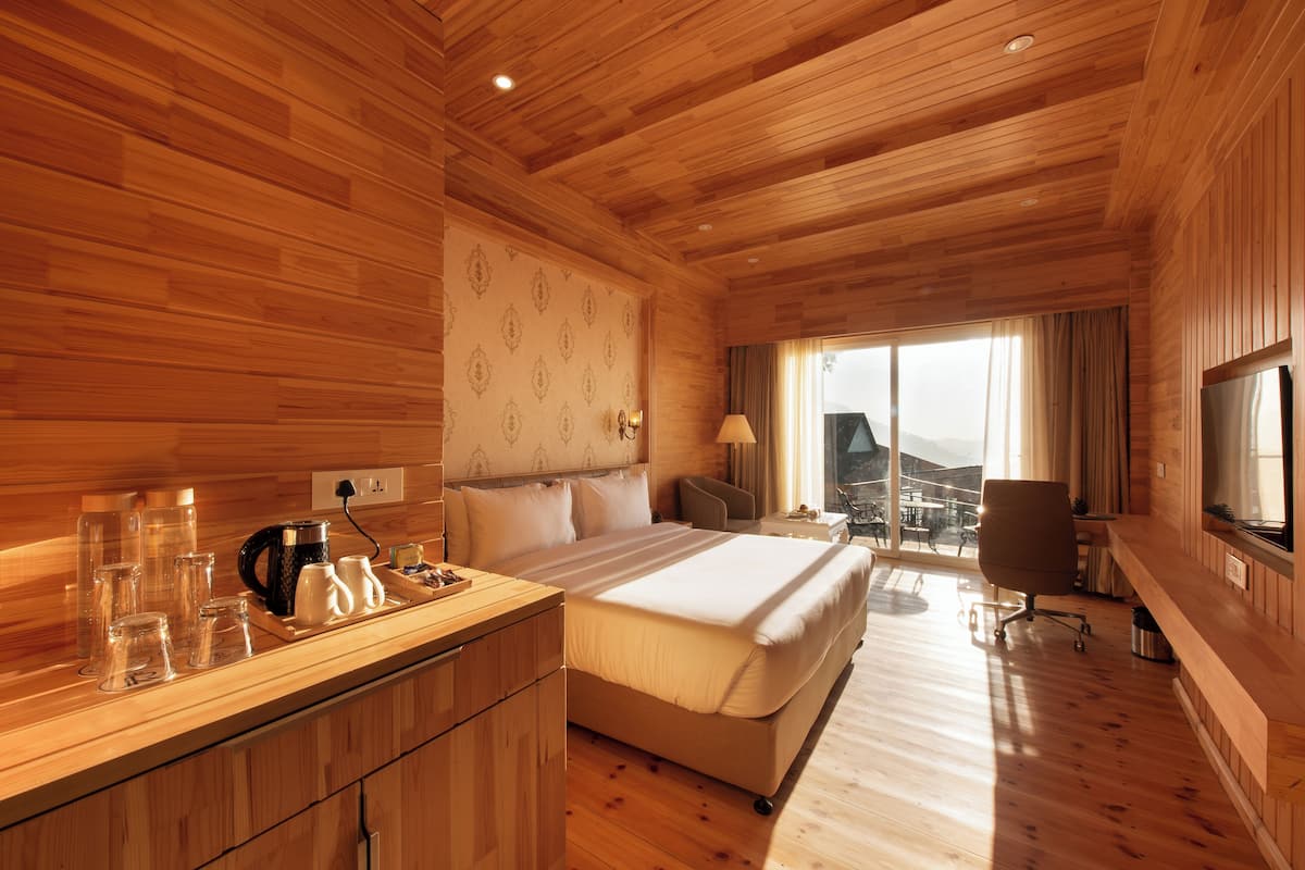 Ein Zimmer mit Holzwänden, einem Bett, einem Nachttisch, einer Lampe und Blick ins Freie.