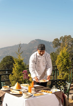 A chef serving food at an outdoor table with a mountain view.