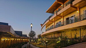A hotel with a curved facade, outdoor seating area, and a well-lit entrance. - Royalpine Rosastays Kasauli (Kasauli)