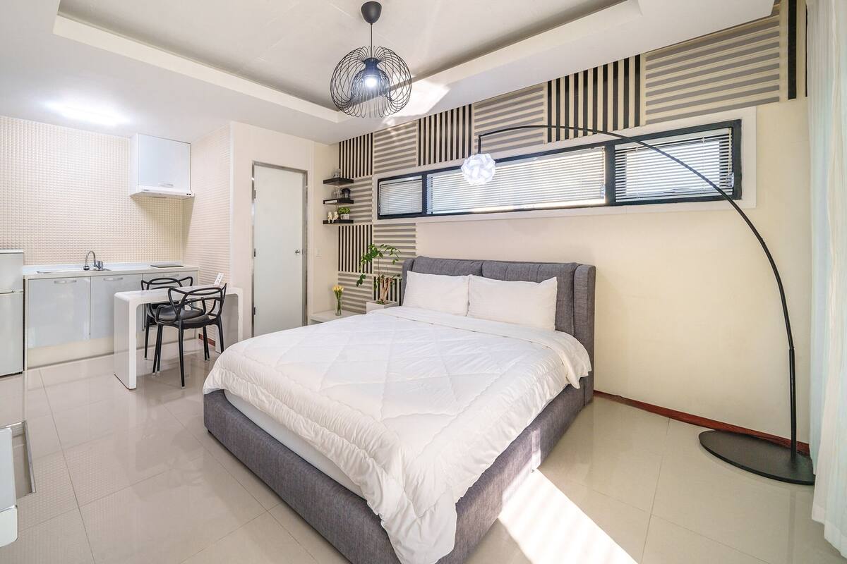 A modern bedroom with a bed, bedside table, and a small desk with a chair.