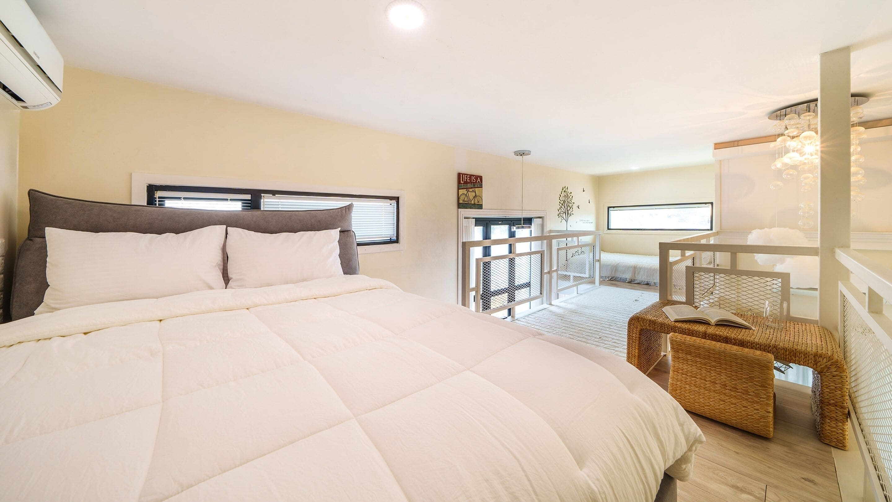 A bedroom with a large bed, a window, and a balcony with a wicker chair.