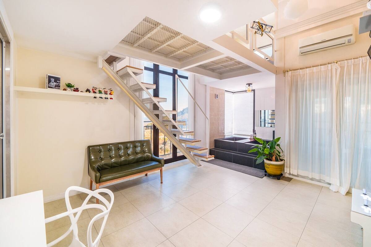 A modern living room with a staircase, a green sofa, a potted plant, and a flat-screen TV.