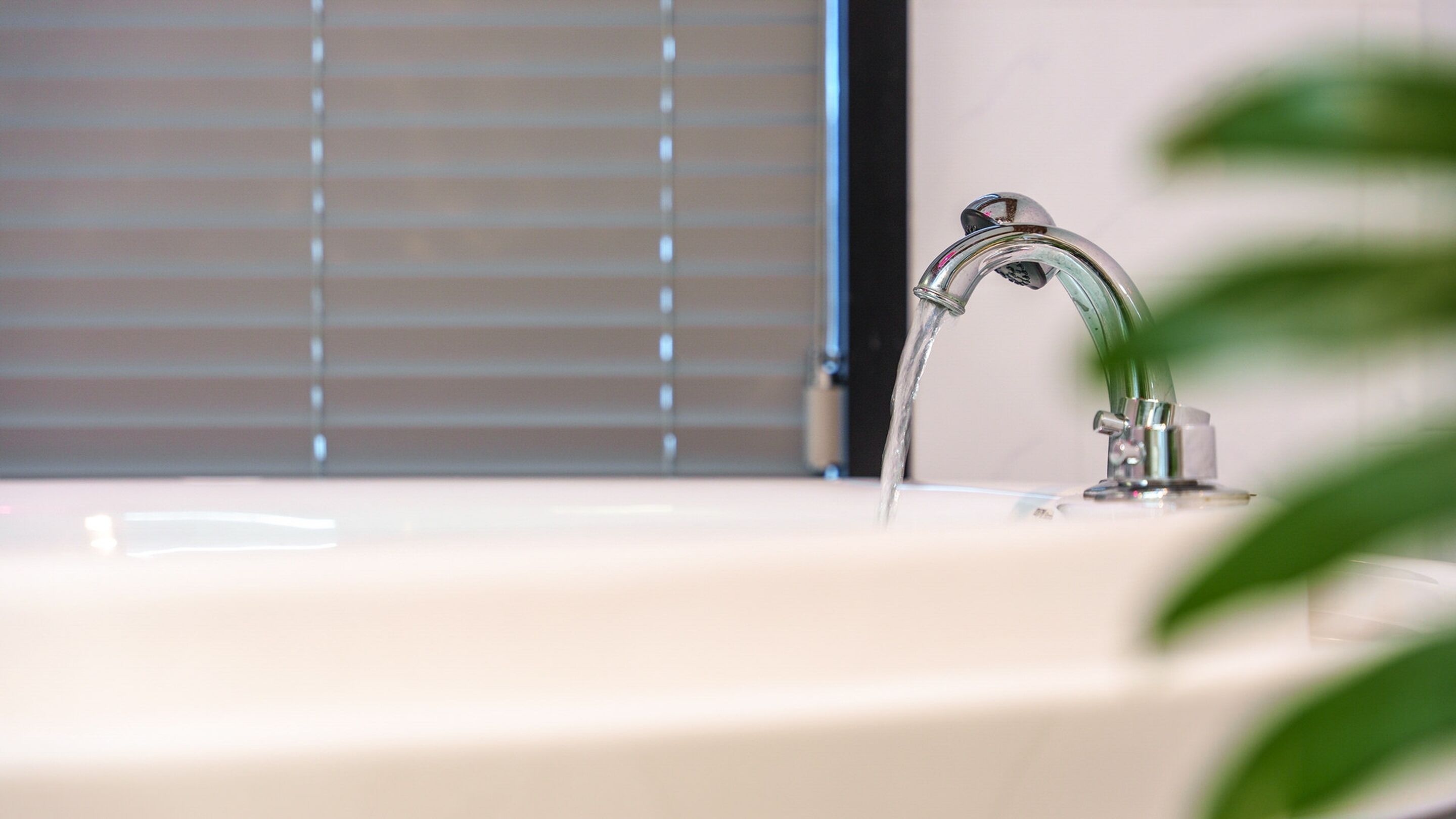 Un lavabo de salle de bain avec un robinet moderne et une fenêtre avec des stores en arrière-plan.