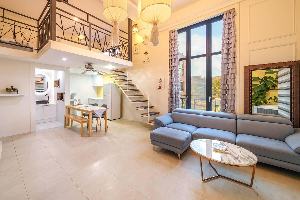 A spacious living area with a sofa, a dining table, and a staircase leading to an upper level.