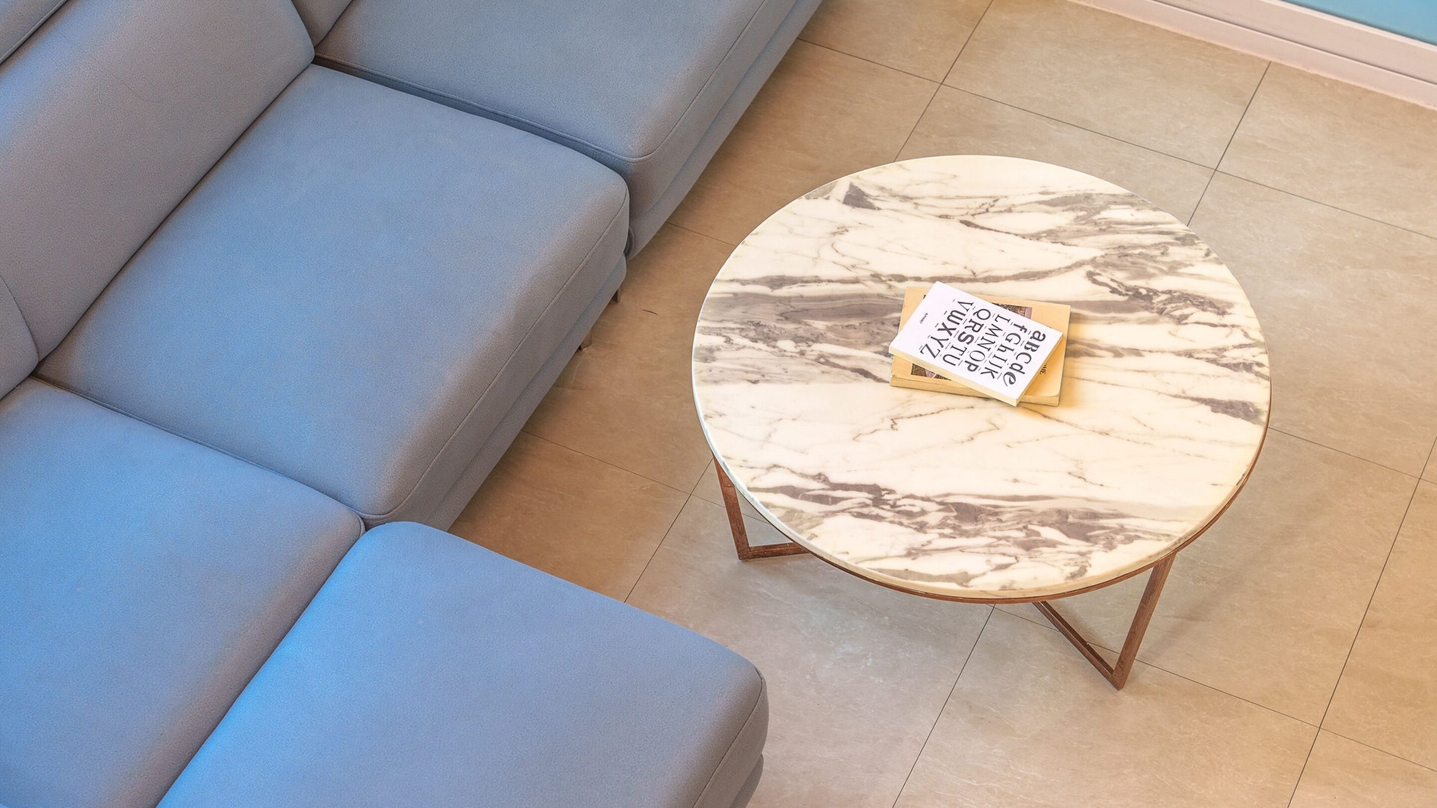 A round marble coffee table with a book on it, placed in front of a grey sofa.
