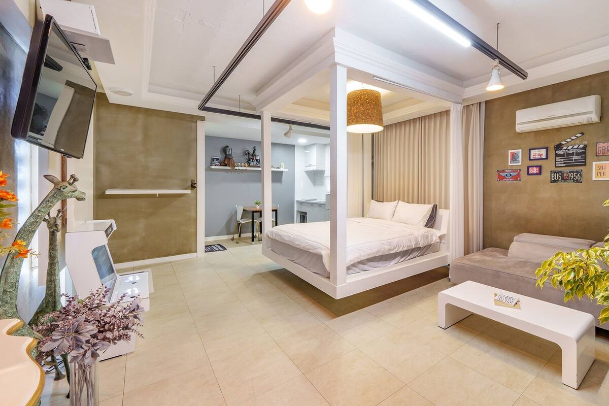 A modern hotel room with a bed, a sofa, a TV, and a desk.