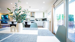 A modern kitchen with white cabinets, a dining area with a table set for four, and a large window providing a view of the outdoors.