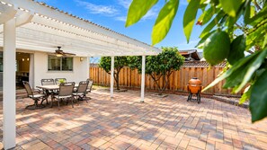 Un patio con una pérgola, una parrilla y una mesa de comedor con sillas.