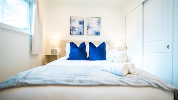 A hotel room with a bed, two bedside tables, a window, and two abstract paintings on the wall.
