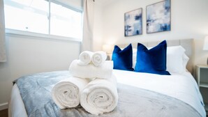 A neatly made bed with rolled white towels and blue pillows, a bedside lamp, and artwork on the wall.