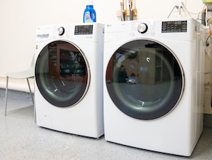 Two white front-loading washing machines with control panels, placed on a speckled floor.
