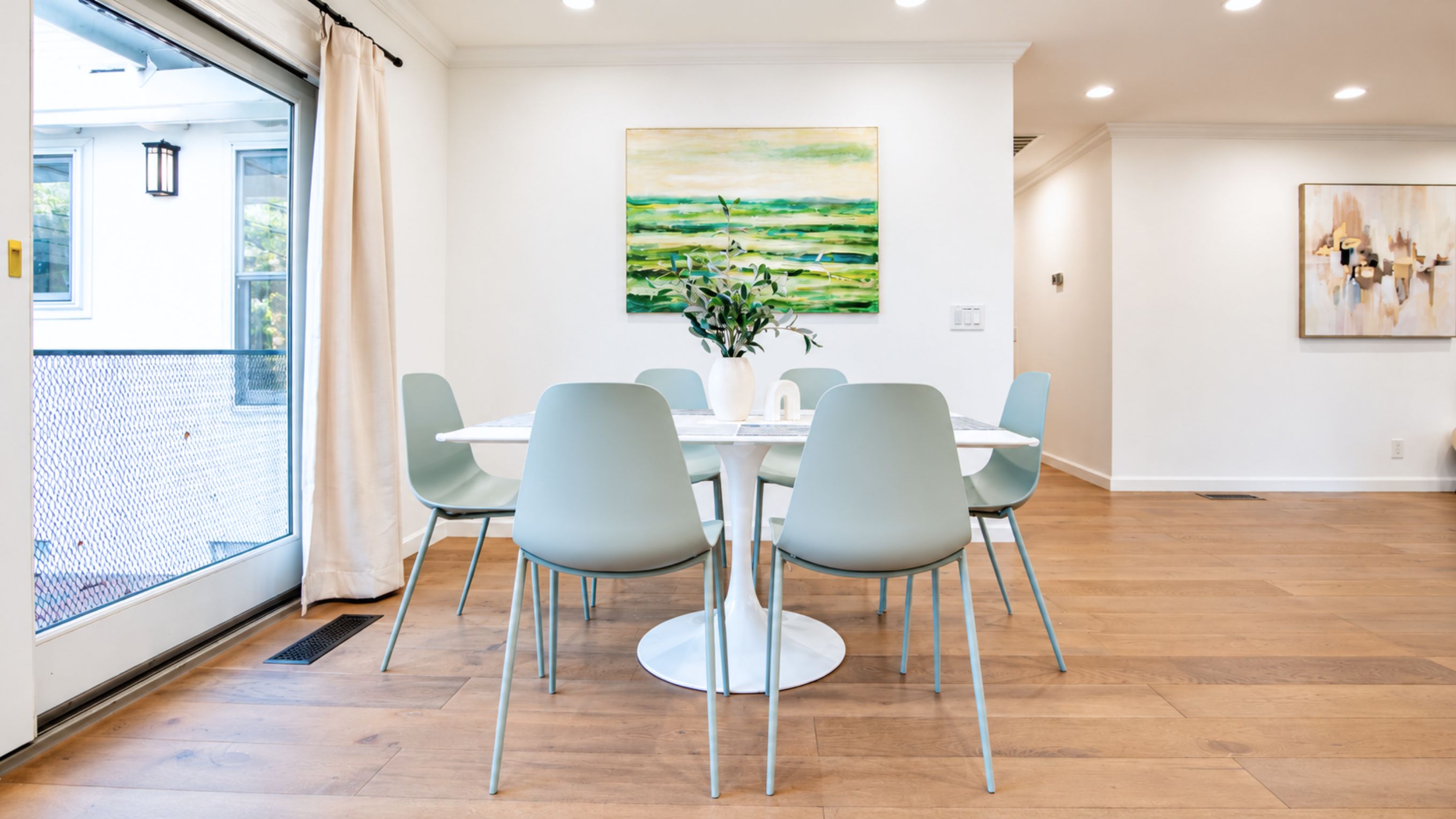 A dining area with a round table, four chairs, a vase with flowers, and two paintings on the walls.