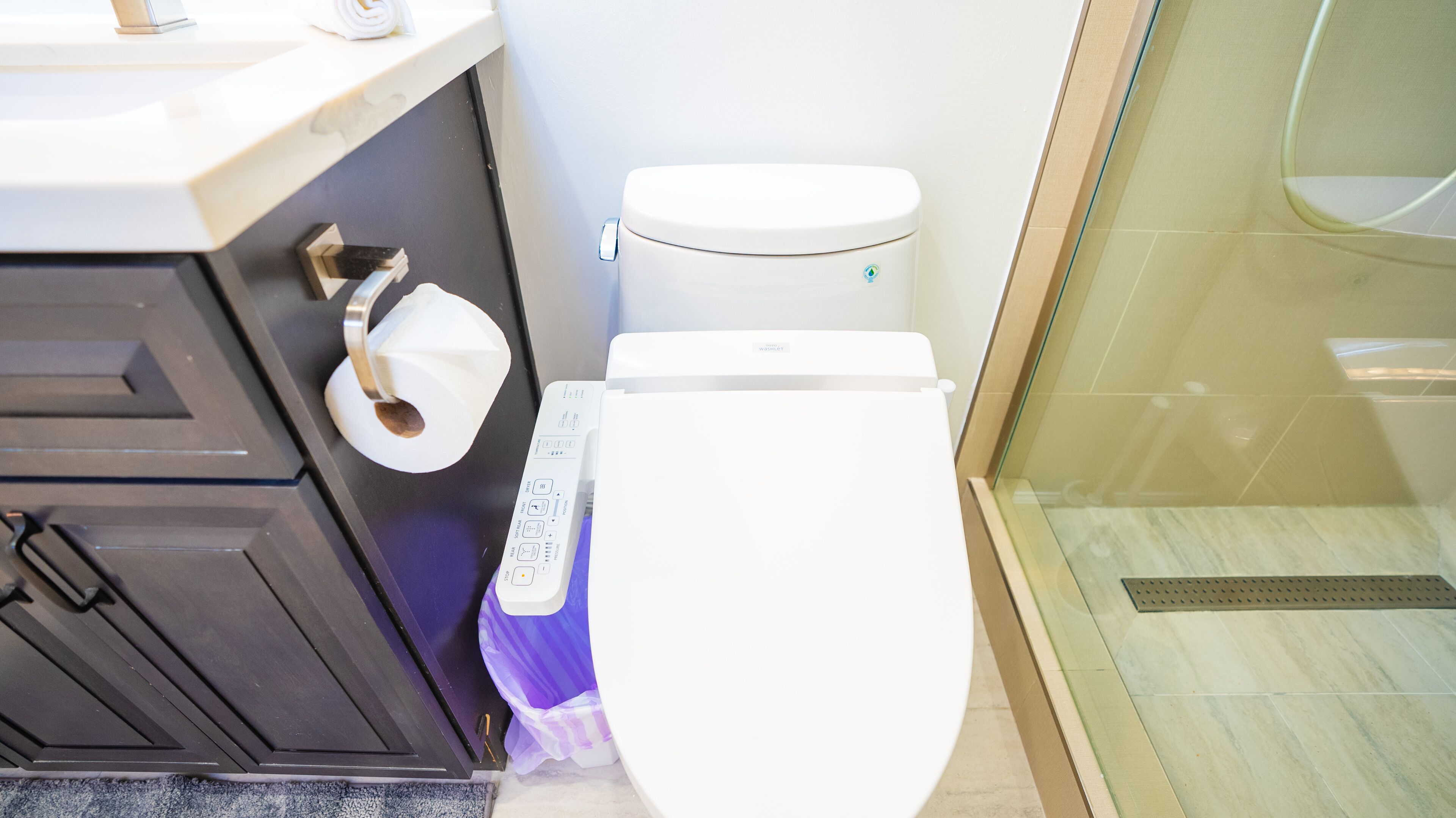 Ein Badezimmer mit Toilette, Papierhandtuchhalter und einer Duschkabine aus Glas.