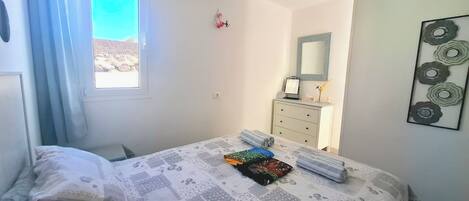 Une chambre à coucher comprenant un lit, une commode, une fenêtre avec des rideaux, un miroir et une œuvre d’art murale.