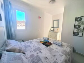 Una camera da letto con un letto, una cassettiera, una finestra con tende, uno specchio e un quadro appeso al muro.