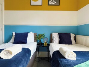 Ein Hotelzimmer mit zwei Betten, einem kleinen Tisch mit Lampe und einem Schild mit der Aufschrift 'BACK' an der Wand.