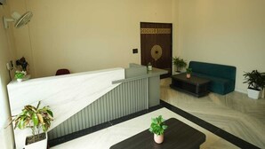 Ein Empfangsbereich mit einer Marmor-Theke, einem dunklen Sofa und Topfpflanzen.