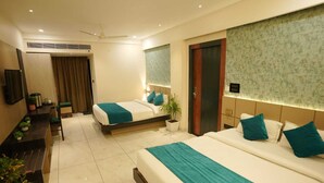 Ein Hotelzimmer mit zwei Betten, einem Schreibtisch, einem Sessel, einem Fernseher und einer Zimmerpflanze.