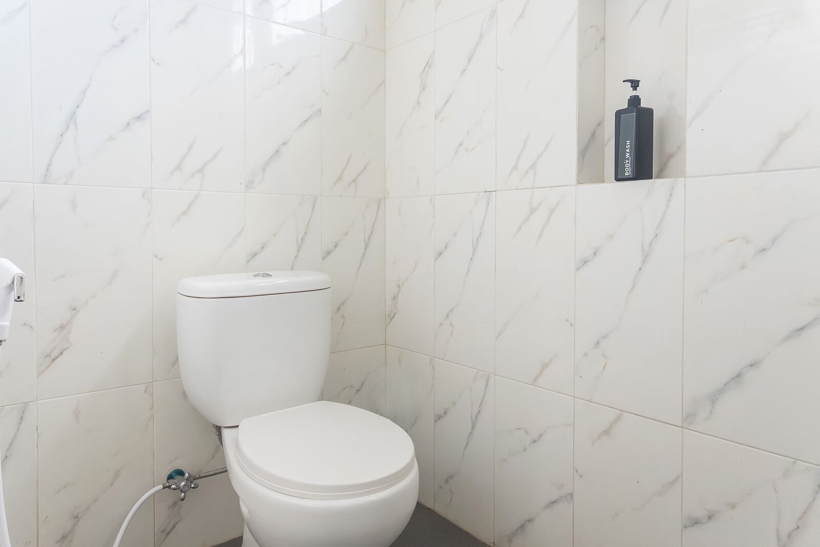 A bathroom with a white toilet, marble tiles, and a bottle of body wash on the wall.