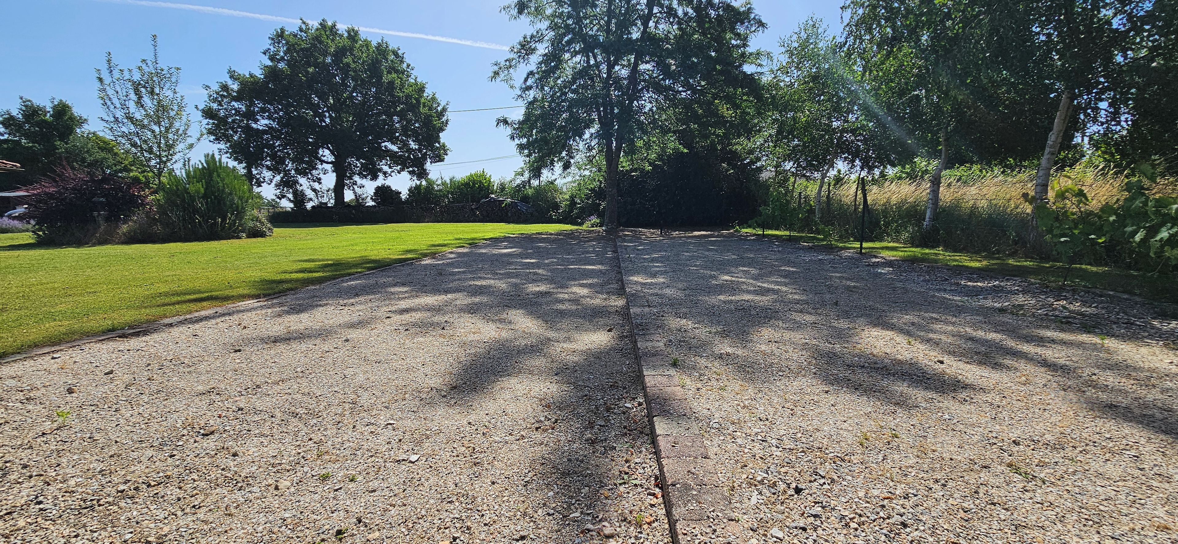 Een grindpad dat leidt naar een huis, met een gazon aan de ene kant en bomen aan de andere kant.