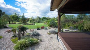A covered outdoor area with a gravel path, various plants, and a lawn. - Country cottage (Linards)