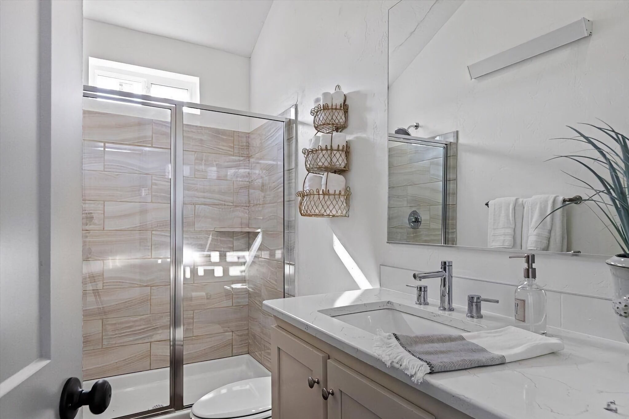 Un baño moderno con cabina de ducha de vidrio, un lavamanos blanco con encimera de mármol y un espejo grande.