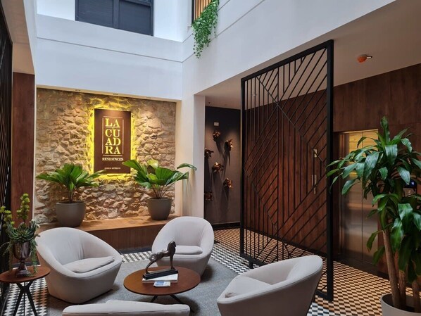 Un lobby moderno con pared de piedra, dos plantas en macetas y una zona de estar con dos sillones y una mesa de centro.