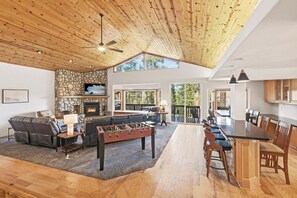A spacious living area with a stone fireplace, a foosball table, and a large seating area. - Tree Top Haven: Private Forest in Backyard! Forest & Peek-a-Boo Lake Views! Foosball! FREE EV CHARGER! Walking Distance to Lake and Village! (Big Bear Lake)