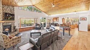 Ein großzügiger Wohnbereich mit Kamin, Ledersofas, Holzboden und großen Fenstern mit Blick ins Freie.